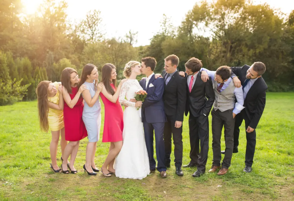 Portrait Of Newlywed Couple Kissing Posing With Bridesmaids And Groomsmen