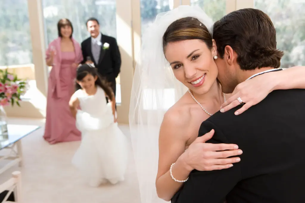 Newlyweds Enjoying an Intimate Hug with Family Celebrating in the Background
