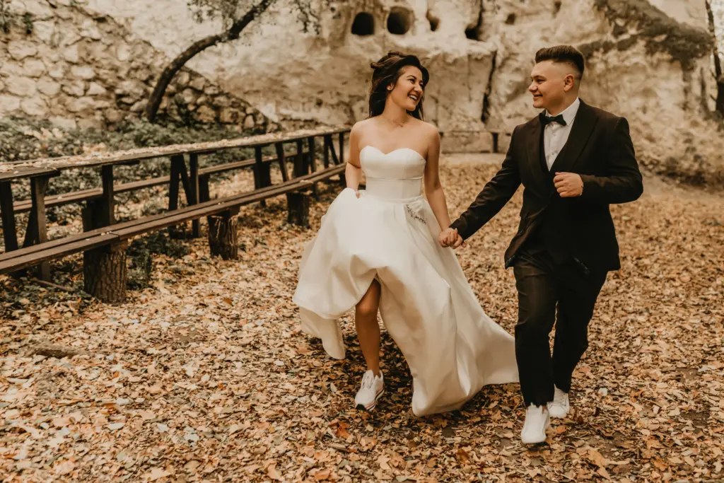 Newlyweds Running Hand-in-Hand Through a Forest of Autumn Leaves
