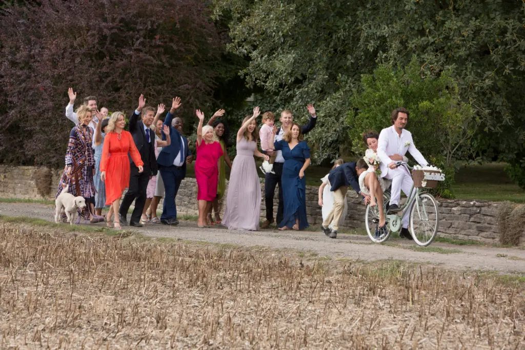 Wedding guests waving off newlyweds on bicycles